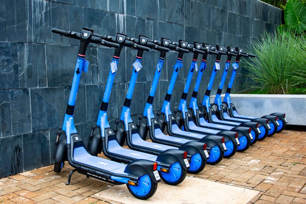 Bright blue electric scooters neatly lined up against a wall in Londrina, Brazil.